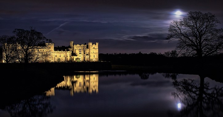 night time view of Raby Castle and surrounding deer park reflected in a lake.